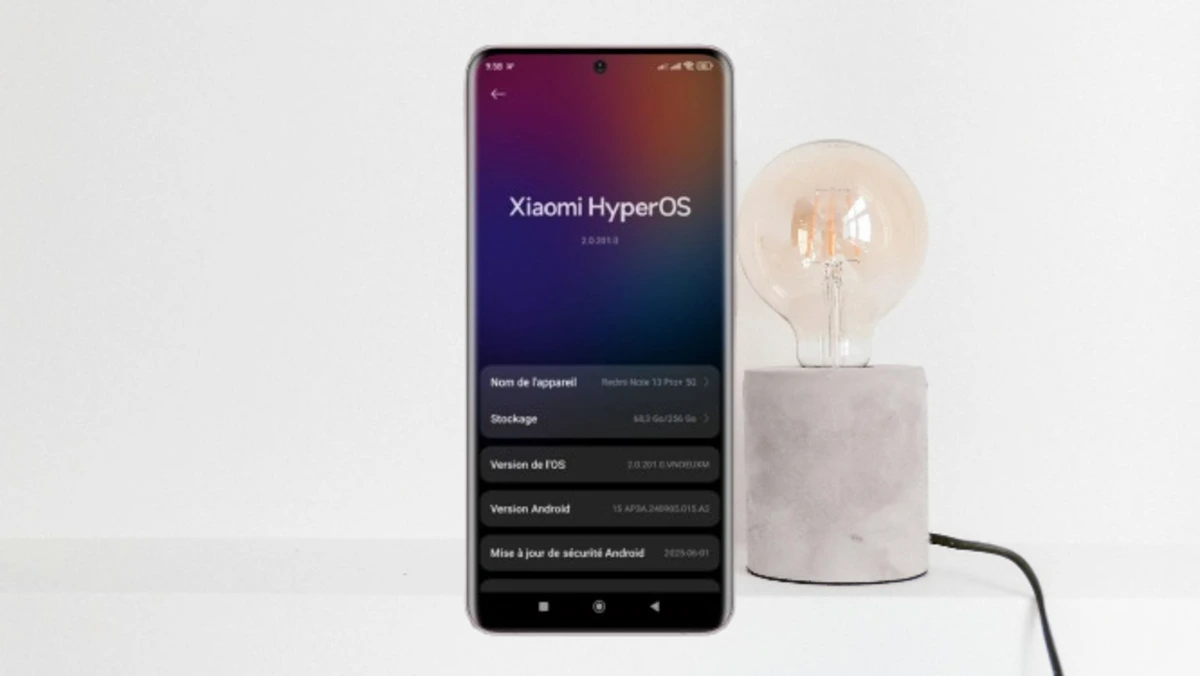 Smartphone mostrando a tela de informações do Xiaomi HyperOS ao lado de uma luminária moderna.