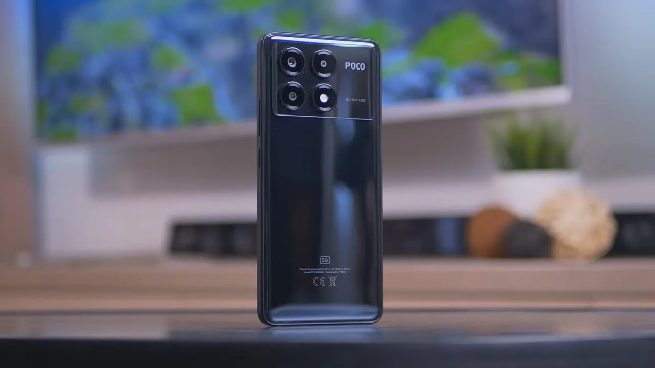 POCO X6 Pro Recebe HyperOS 2.2 Global Estável: Câmera 6.0 e Novas Funcionalidades 5 Smartphone POCO X6 Pro na cor preta, exibindo a parte traseira com o módulo da câmera retangular, que possui quatro lentes circulares e as inscrições 'POCO' e '64MP OIS', sobre uma superfície de madeira e fundo desfocado.