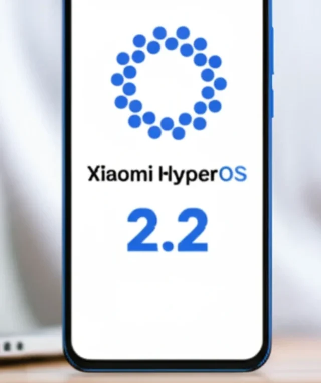 Smartphone mostrando a tela com o logo do Xiaomi HyperOS e o número 2.2, sobre uma mesa de madeira com um laptop e uma mão usando um mouse sem fio. Foco no smartphone.