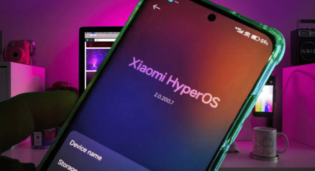 Uma mão segura um smartphone com uma capa protetora verde fluorescente, exibindo a tela "Xiaomi HyperOS" com a versão 2.0.200.7. Ao fundo, um ambiente de mesa iluminado por luzes roxas e rosas, mostrando um monitor de computador, uma câmera retrô e outros objetos eletrônicos.