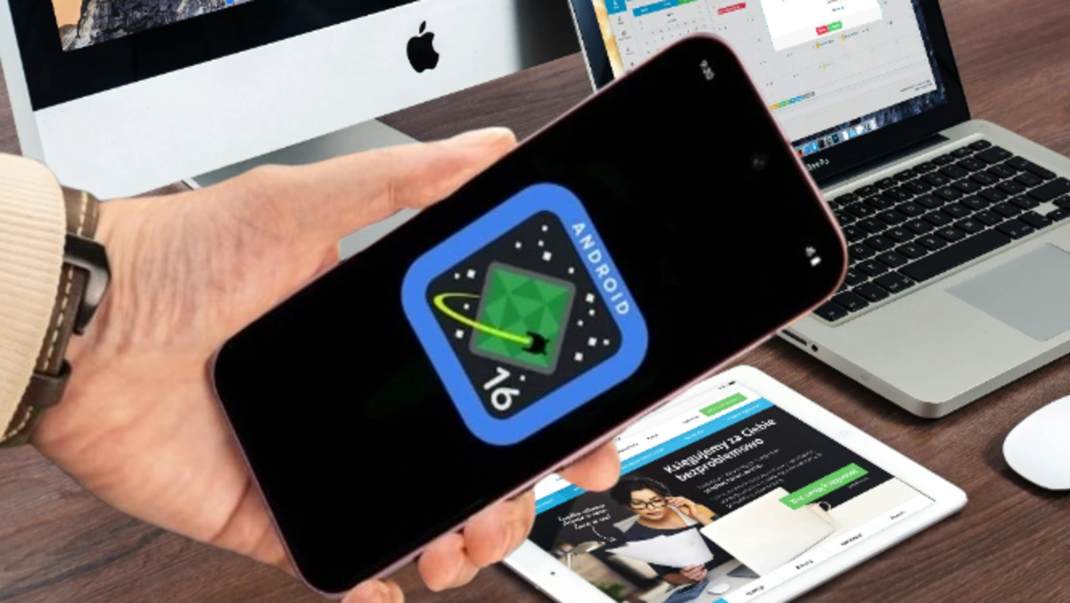 Mão segurando smartphone com o logo do Android 16, com um iMac, MacBook e tablet ao fundo, representando a integração de novas tecnologias.
