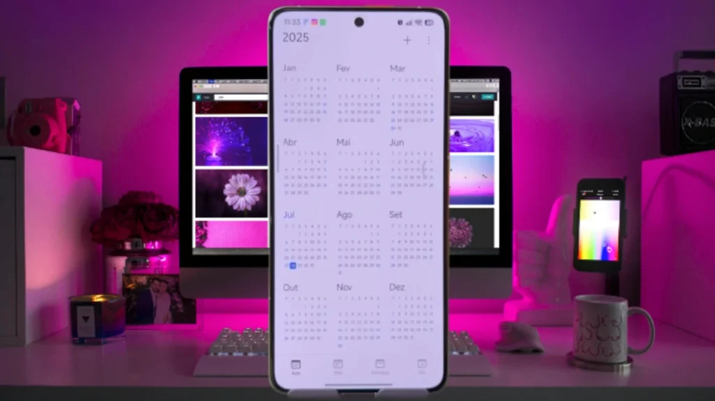 Smartphone Xiaomi com o aplicativo de calendário do HyperOS 3 exibindo o ano de 2025 completo, em um ambiente de trabalho com iluminação roxa.