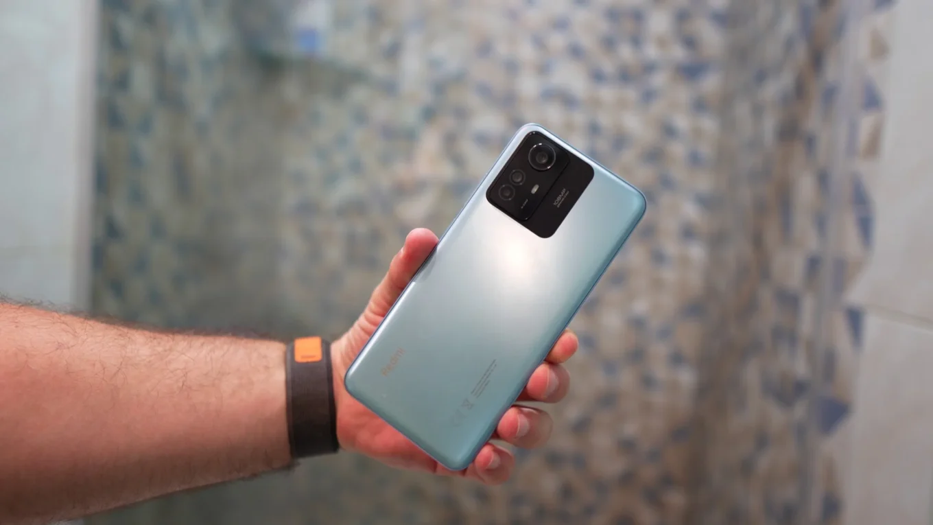Mão segurando um smartphone Redmi Note 12S azul-claro, exibindo a câmera traseira com a menção de 108MP, pronto para a experiência HyperOS 2.2.