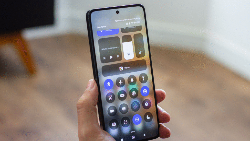 Android 16 chega aos dispositivos Xiaomi: testes já começaram para Redmi e POCO. Na imagem, um smartphone Xiaomi, possivelmente um modelo recente com a tela ligada, exibindo a central de controle e notificações. A interface mostra botões para Wi-Fi, Bluetooth, lanterna, modo de economia de energia, entre outros. A imagem foca na tela do celular, que é segurado pela mão de uma pessoa.