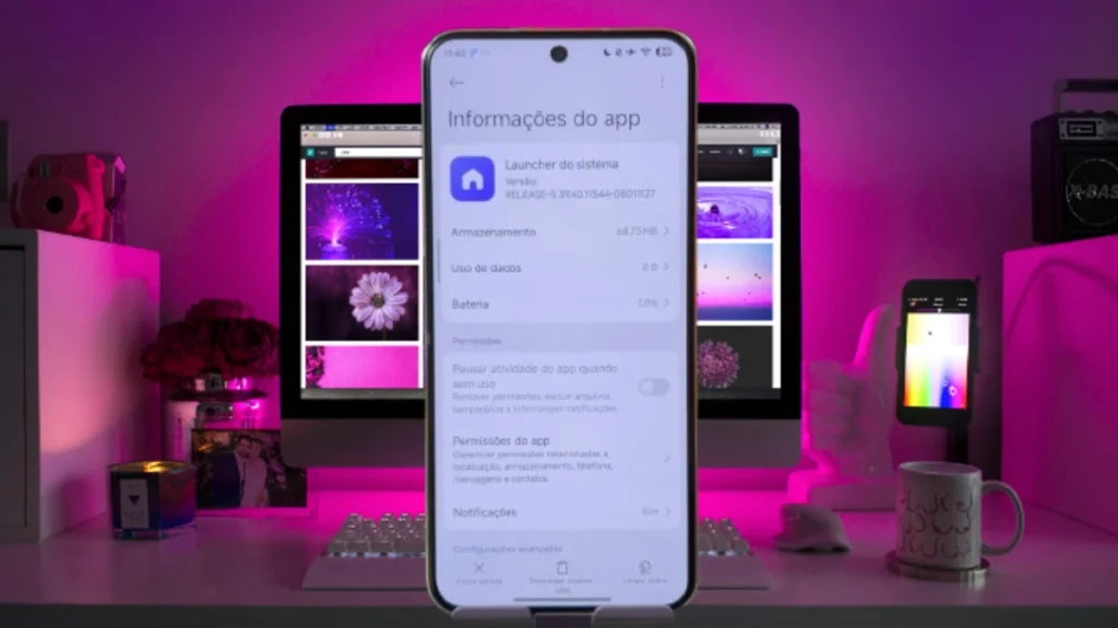 Uma imagem de close-up da tela de um smartphone exibindo a página de "Informações do app" para o "Launcher do sistema" da Xiaomi, mostrando a versão "RELEASE-S-394031154-08011127" em um ambiente de mesa de trabalho com iluminação rosa, que pode ser tanto o **HyperOS Launcher e Poco Launcher**.