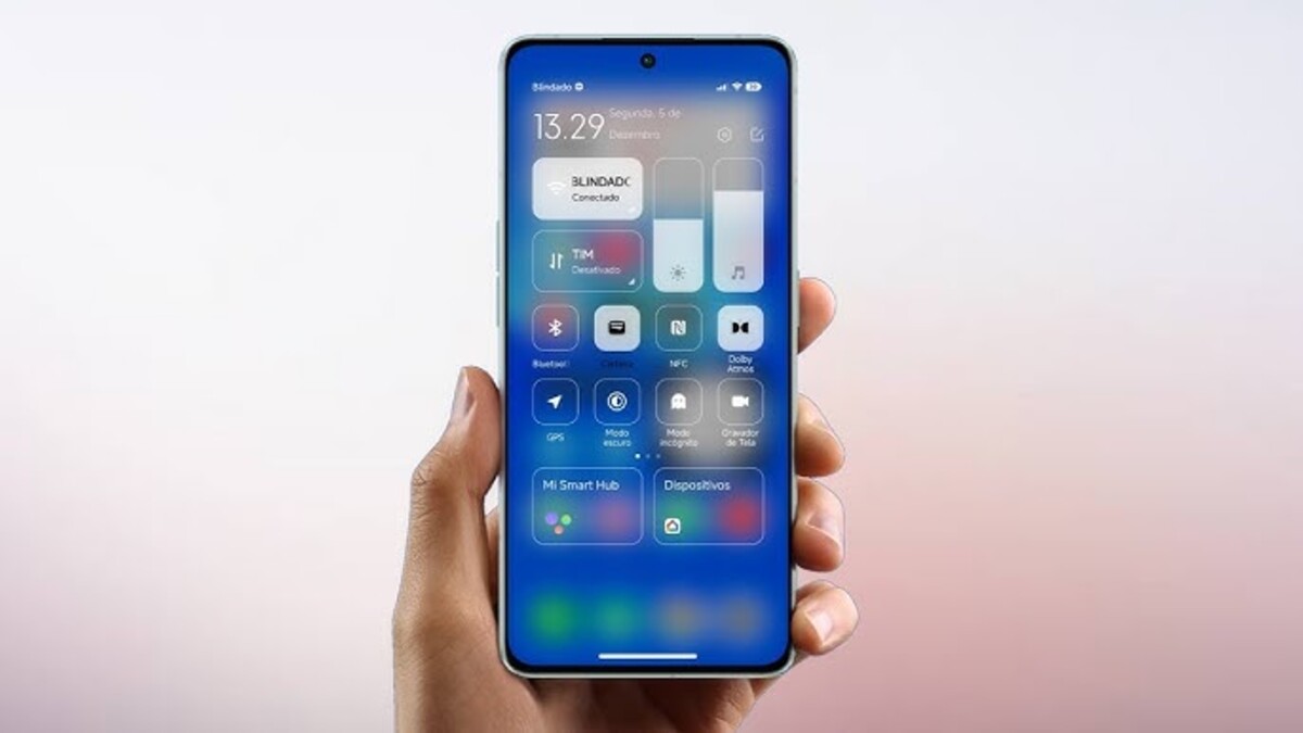 Uma mão segura um smartphone Xiaomi que exibe a nova Central de Controle do HyperOS Launcher, com seu design moderno e minimalista em tons de azul e branco, mostrando controles de brilho e volume e atalhos rápidos. Este visual também é um destaque no Poco Launcher.
