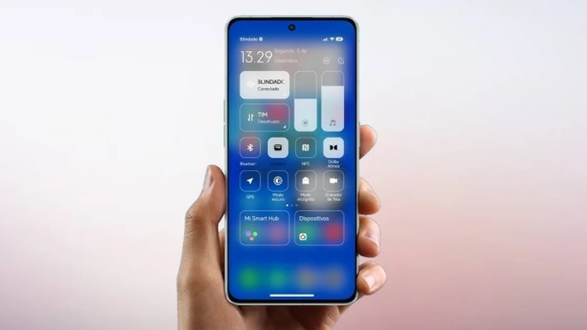 Uma mão segura um smartphone Xiaomi que exibe a nova Central de Controle do HyperOS Launcher, com seu design moderno e minimalista em tons de azul e branco, mostrando controles de brilho e volume e atalhos rápidos. Este visual também é um destaque no Poco Launcher.