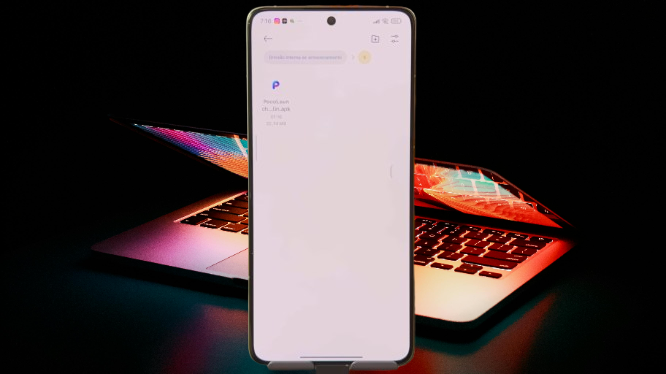 Smartphone exibindo o arquivo de instalação do POCO Launcher, um dos novos apps do HyperOS 2.2, com um laptop brilhando ao fundo.