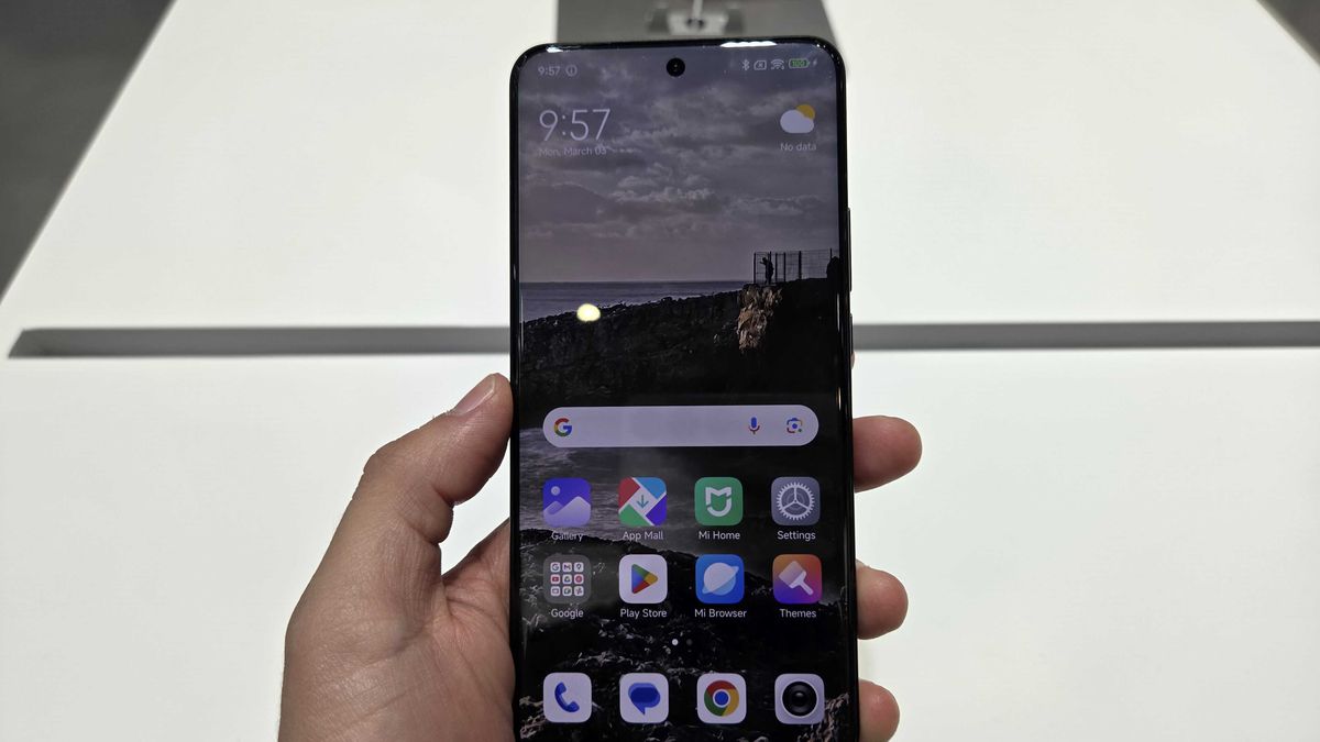 HyperOS 3 Global: Xiaomi lança atualização primeiro nos celulares intermediários 1 Mão segurando um smartphone Xiaomi exibindo a tela inicial com o sistema HyperOS 3. O papel de parede escuro (noturno) mostra uma paisagem de penhascos e nuvens, com ícones coloridos de aplicativos.