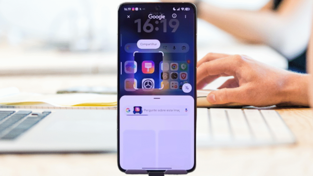 Smartphone exibindo a tela inicial do HyperOS Launcher 3 com a funcionalidade de Pesquisa Visual do Google ativada, mostrando uma prévia da tela e opções para interagir com a imagem, com uma pessoa trabalhando em um computador ao fundo.