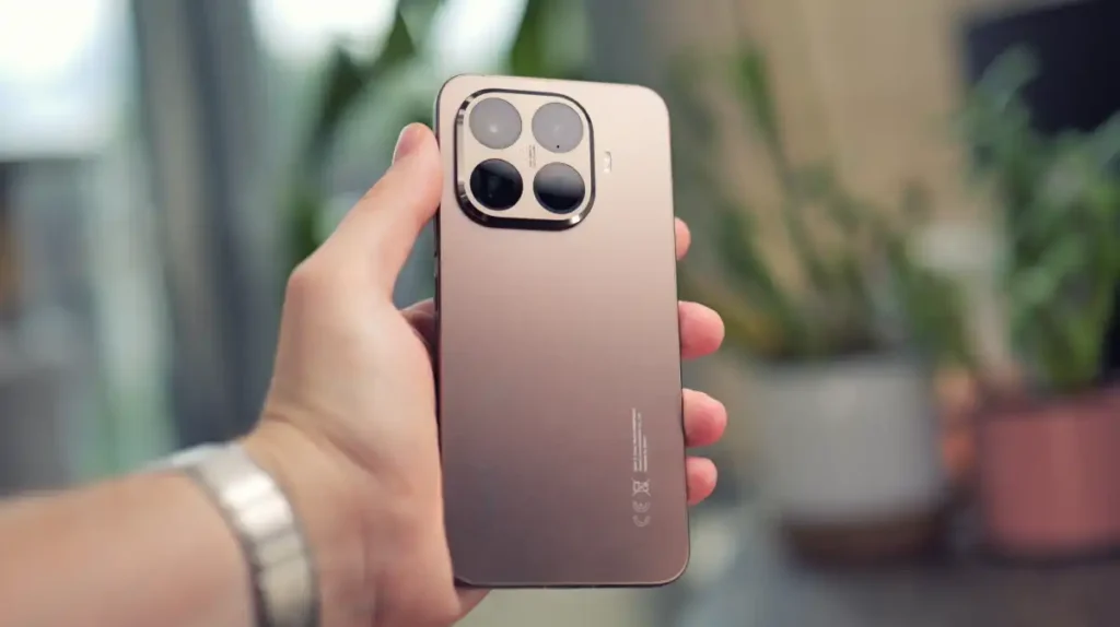 Smartphone Xiaomi 15T Pro na cor marrom segurado por uma mão, exibindo o módulo de câmera quádrupla traseiro. Este é um dos primeiros dispositivos a receber a atualização HyperOS 3 Global.